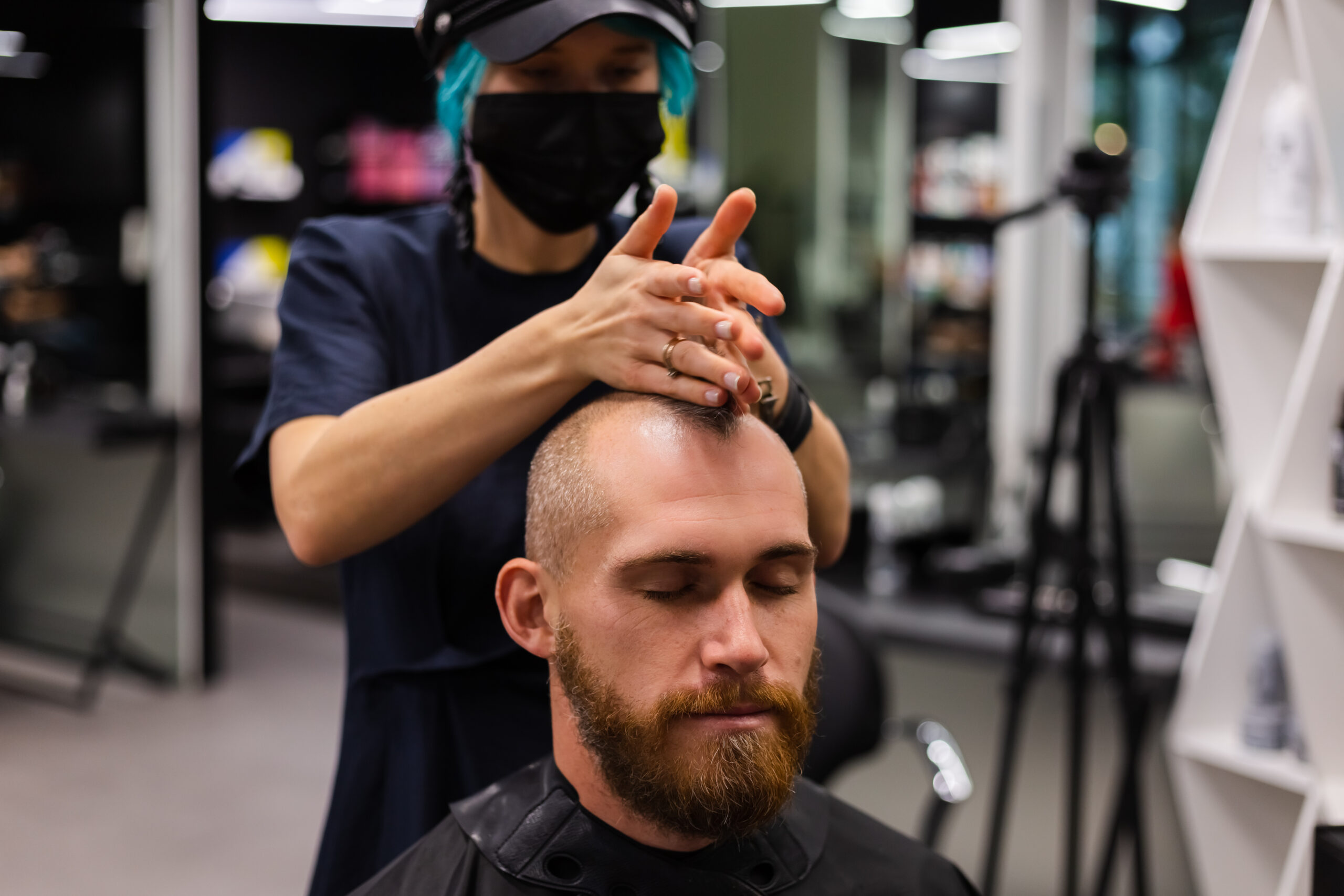 professional hairdresser wearing protective face mask, make haircut for european bearded brutal man in beauty salon